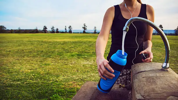 Female runner fills up water bottle outdoors at the public park