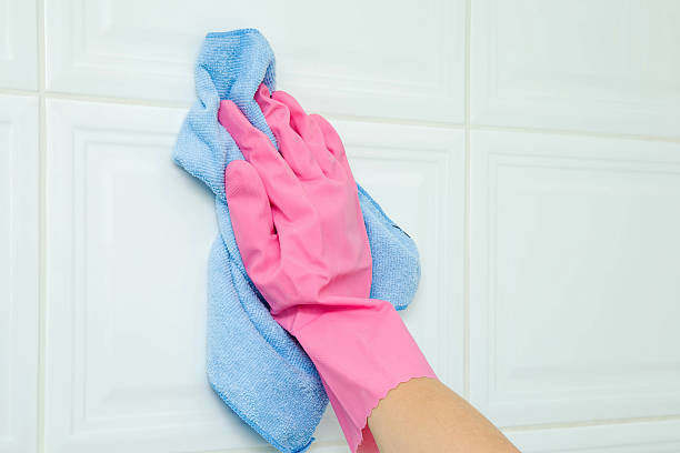 istock Hand in protective glove cleaning white tiles with blue rag. 621933044