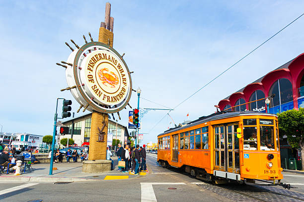 Fisherman's Wharf Sign San Francisco Cable Car San Francisco, United States - May 5, 2016: Orange vintage Swiss F Market streetcar rolls by large sign at entrance to the tourist attraction of Fisherman's Wharf on the corner of Beach and Jones Street. Horizontal fishermans wharf stock pictures, royalty-free photos & images