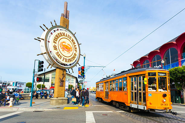Fisherman's Wharf Sign San Francisco Cable Car San Francisco, United States - May 5, 2016: Orange vintage Swiss F Market streetcar rolls by large sign at entrance to the tourist attraction of Fisherman's Wharf on the corner of Beach and Jones Street. Horizontal fishermans wharf san francisco photos stock pictures, royalty-free photos & images