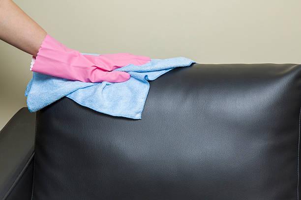 istock Hand in pink protective glove wiping leather sofa with cloth. 621933868