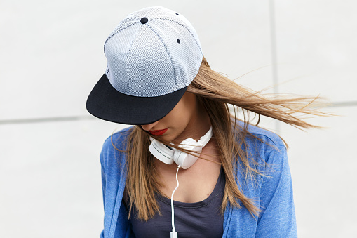 Portrait of young woman with cap and headphones looking down.