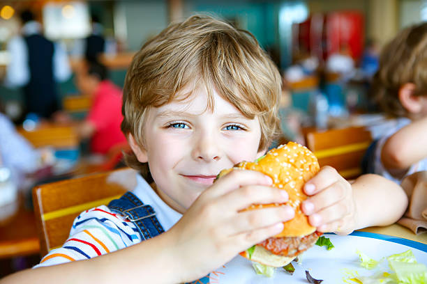 istock Cute healthy preschool boy eats hamburger sitting in cafe outdoo 621973206