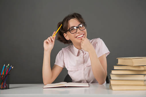 Cute, caucasian, nerd girl sitting at the desk with a pencil in her hand and books in front of her