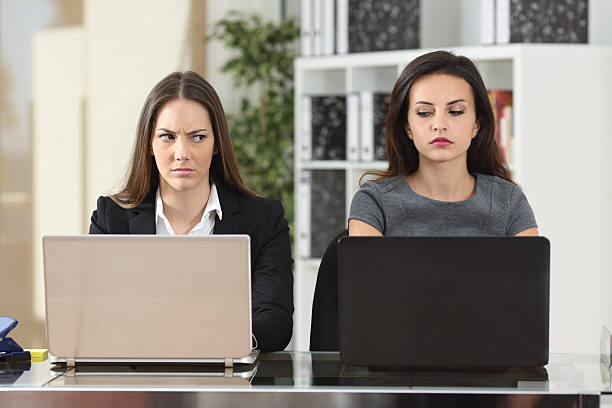 Angry businesswomen looking with hate Front view of two angry businesswomen looking each other with hate working with laptops at office envy stock pictures, royalty-free photos & images