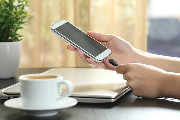 Girl hand connecting charger to smart phone Girl hand connecting charger to smart phone in a table at home with a window in the background phone charger cable stock pictures, royalty-free photos & images