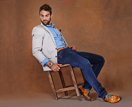 Shot of a stylishly dressed young man sitting against a brown background