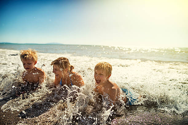 istock Mother and sons lying on beach splashing in sea waves 621982034