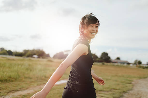 Woman runner walking on field in morning Outdoor shot of smiling young woman runner looking at camera. Chinese female walking on field in morning. looking over shoulder stock pictures, royalty-free photos & images