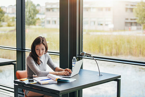 istock Young asian woman in library doing assignments 621989962