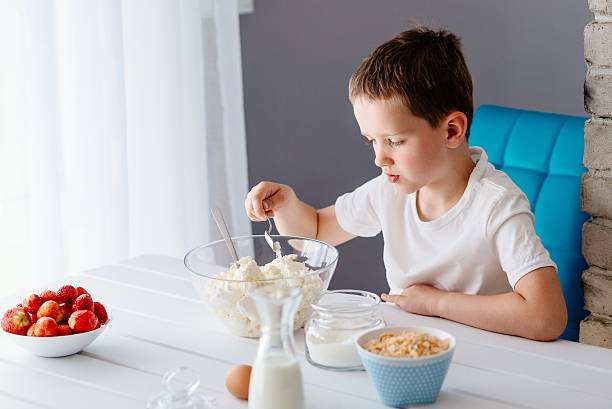 istock Boy adding sugar to white cheese in bowl for cheesecake. 621993174