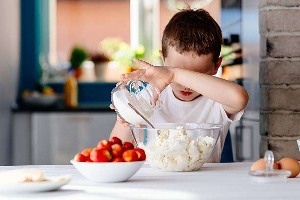 istock Boy adding sugar to white cheese in bowl for cheesecake. 621993350