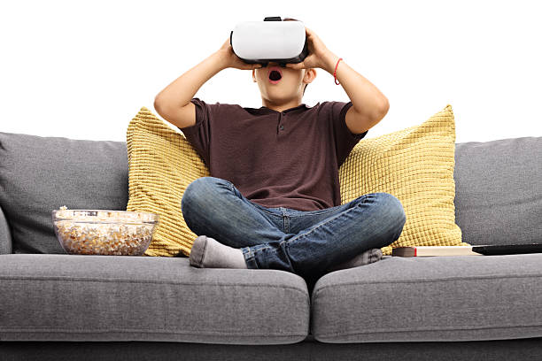 istock Amazed little boy sitting on couch and using VR goggles 621994276