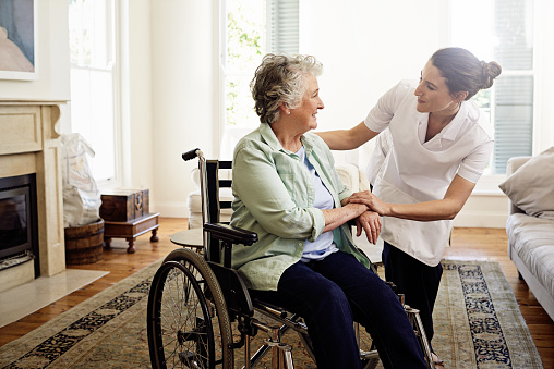 Shot of a smiling caregiver helping a senior woman in a wheelchair at home