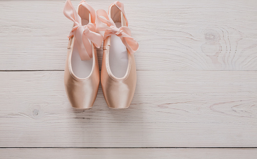 Pastel pink ballet shoes background. New pointe shoes with satin ribbon lay on white rustic shubby chic wood, top view with copy space