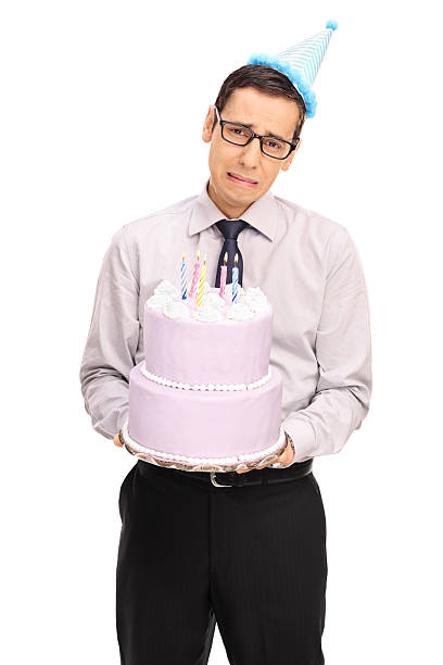 istock Sad young man with party hat holding birthday cake 621995450