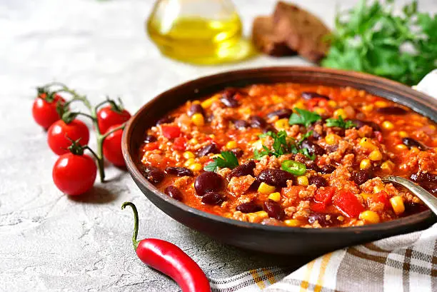 Chili con carne in a clay bowl on a concrete or stone background- traditional dish of mexican cuisine.