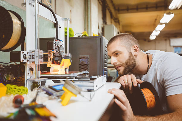 Young man using a 3D printer in a construction workshop Young man using a 3D printer in a construction workshop, holding filamnet in hand. 3d printing filament photos stock pictures, royalty-free photos & images