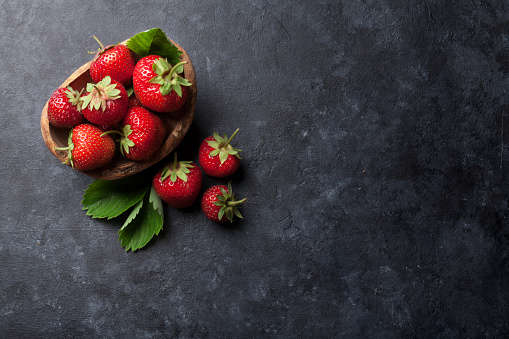 Fresh garden strawberry in bowl on stone table. Top view with copy space