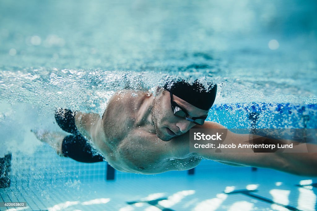 Fit swimmer training in the pool Underwater shot of fit swimmer training in the pool. Professional male swimmer inside swimming pool. Swimming Stock Photo