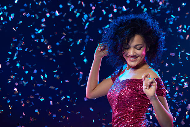 Happy mixed race woman in sequined dress dancing on a party over colorful background with confetti