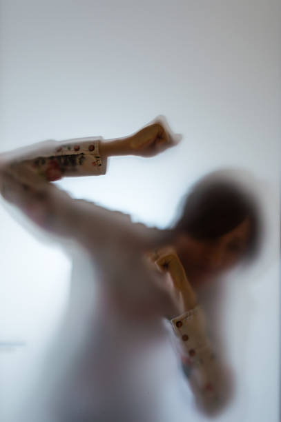 Blurry figure of a woman punching the frosted glass stock photo