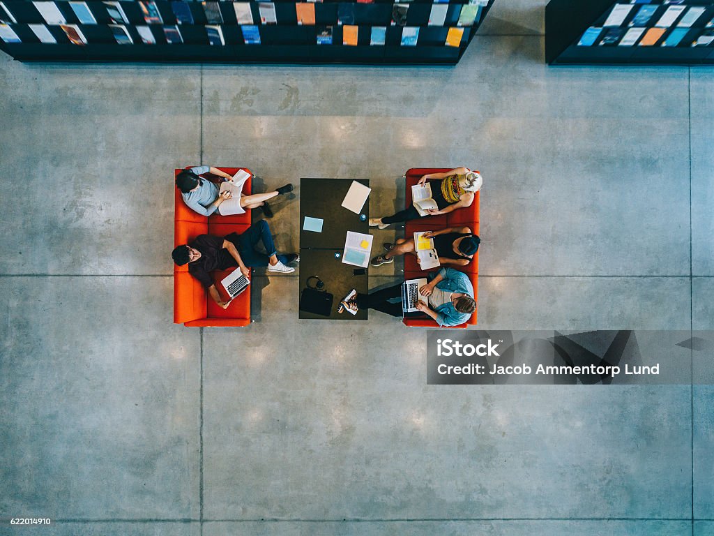 University students sitting in a library Top view of university students sitting in a library with books and laptop. Young people studying together at college library. High Angle View Stock Photo