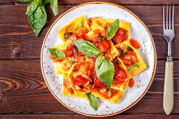 Ravioli with tomato sauce and basil on dark background, top view.