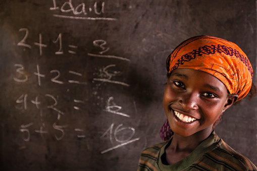 African little girl during math class class in very remote school. The bricks that make up the walls of the school are made of clay and straw. There is no light and electricity inside the classroom