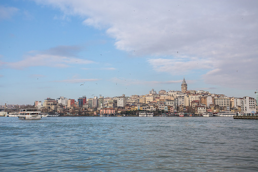 Istanbul,Turkey - January 2, 2015: Galata Tower Amidst Buildings In Front Of River Against Clear Sky In City. Beyoglu area viewed from Eminönü docks, Istanbul, Turkey The Galata Tower (Galata Kulesi in Turkish) — called Christea Turris (the Tower of Christ in Latin) by the Genoese — is a medieval stone tower in the Galata/Karaköy quarter of Istanbul, Turkey, just to the north of the Golden Horn's junction with the Bosphorus.