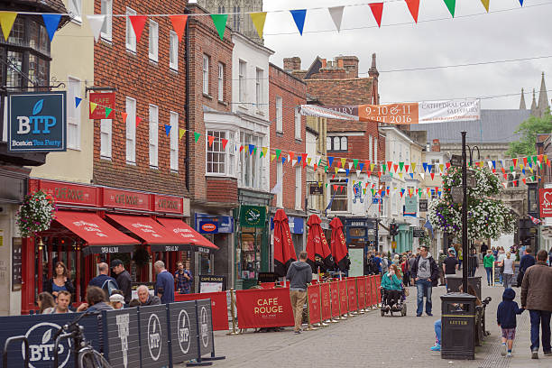 Busy shopping street in Salisbury Salisbury, UK - September 4th 2016: Tourists and shoppers are walking through Salisbury City centre on a Sunday afternoon. Some are sitting down enjoying refreshments and food at tables in the street. high street shops stock pictures, royalty-free photos & images