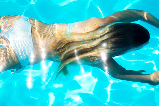 Cute young girl diving in swimming pool. 