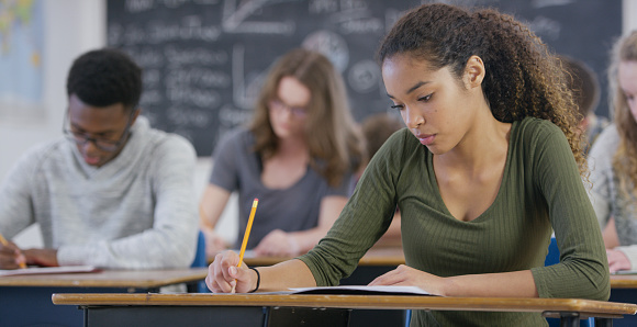 A mixed race teenage girl is taking a high school standardized test in class. She looks down and works on the test.