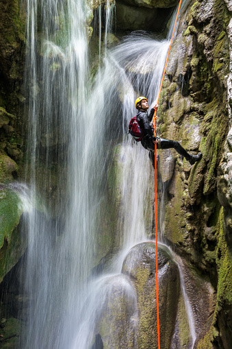 Canyoneering member with backpack rappeling down the waterfall in the canyon.