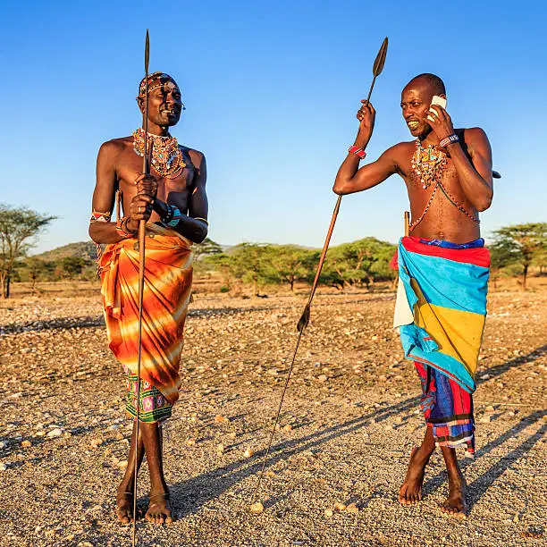 African warrior from Samburu tribe standing on savanna and using a mobile phone, central Kenya. Samburu tribe is one of the biggest tribes of north-central Kenya, and they are related to the Maasai.