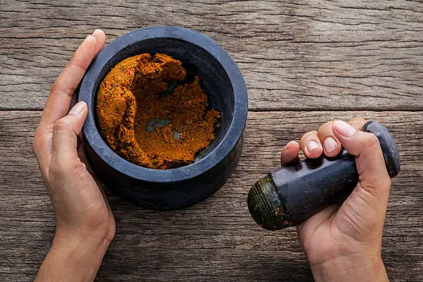 Photo of The women hold pestle with mortar and spice paste .