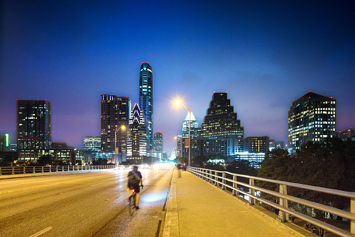 Austin panorama at night on Congess avenue bridge. A biker crosses at high speed while numerous tourists and locals are waiting for the bats to come out.