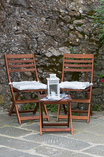 Foldable wooden chairs, mini table with candle lantern on top placing outdoor by stone wall