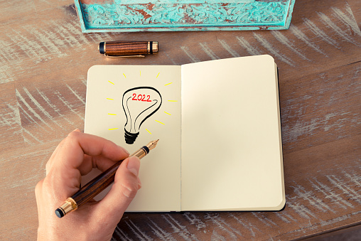 Retro effect and toned image of a woman drawing a lighting bulb with fountain pen on a notebook. Year 2022 symbol for bright idea and business concept, copy space available for text