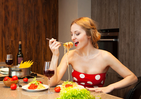 Sexy young blond woman eating spaghetti in the kitchen at home