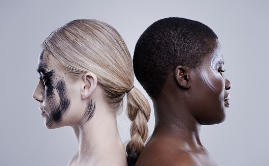 Studio shot of two women standing back to back wearing contrasting makeup