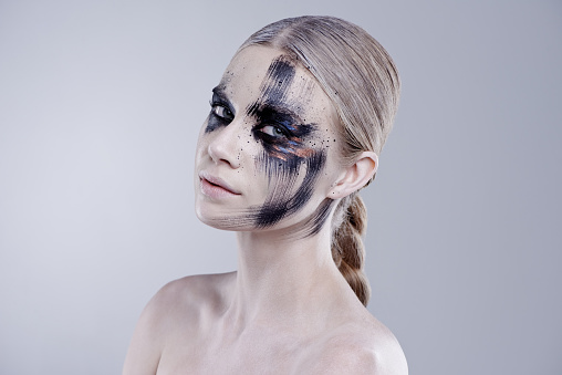 Studio portrait of an attractive young woman wearing creative face paint against a gray background