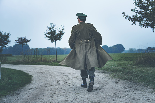 Rear view of vintage 1940s military officer walking on rural road.