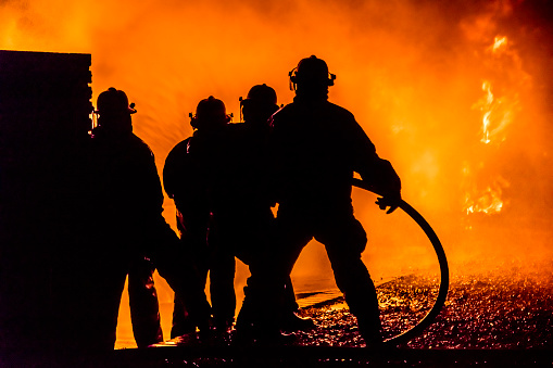 Firefighters silhouette facing the fire with water hoses.