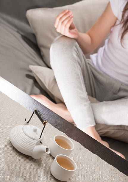 Young woman sitting in meditation pose in front of tea stock photo