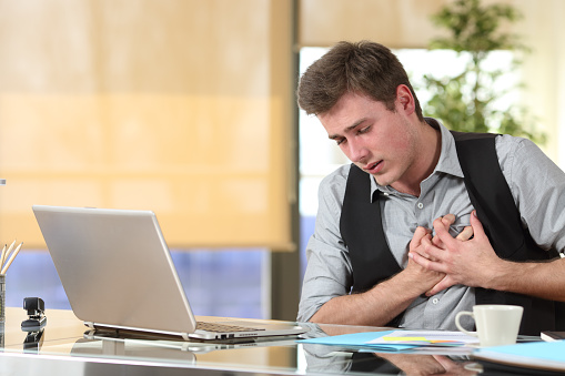 Businessman suffering a heart attack with his hands grabbing the chest sitting in a desktop at office