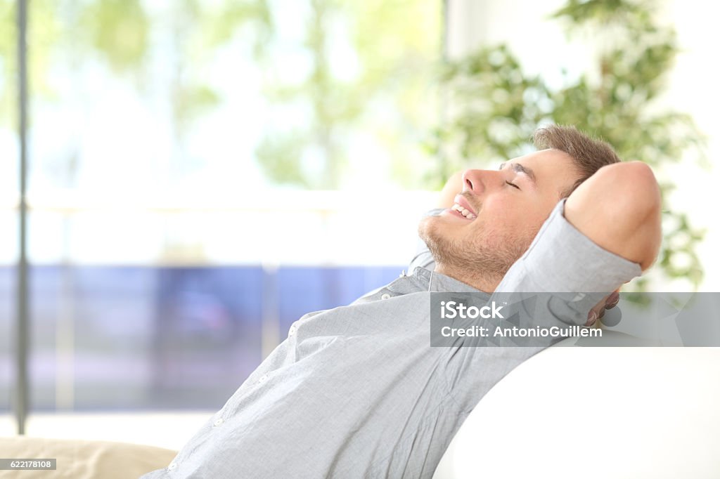 Man resting and breathing at home Side view of a happy attractive man resting and breathing sitting on a couch at home with a window with a green background outdoors Men Stock Photo