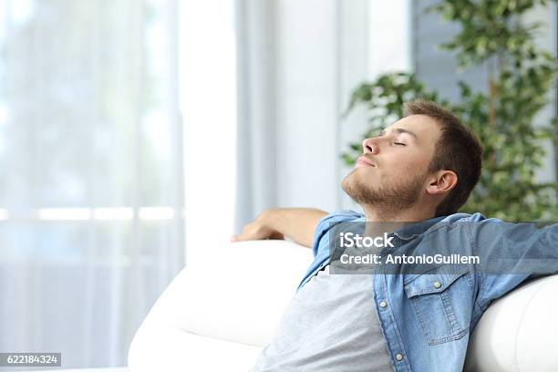 Hombre Descansando En Un Sofá En Casa Foto de stock y más banco de imágenes de Hombres - Hombres, Viento, Ejercicios de respiración