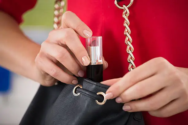 Midsection of woman stealing lipstick at supermarket