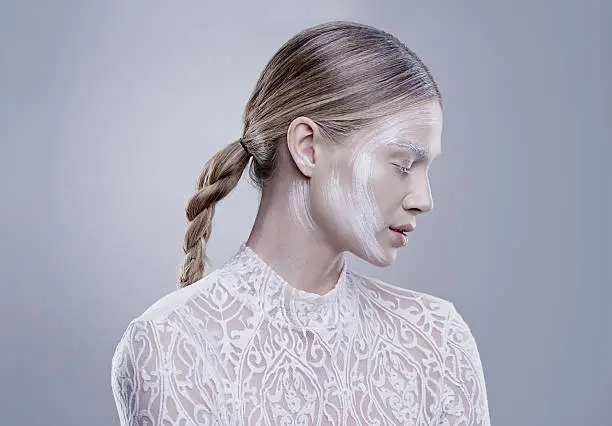Cropped shot of a beautiful young woman with white face paint against a grey background